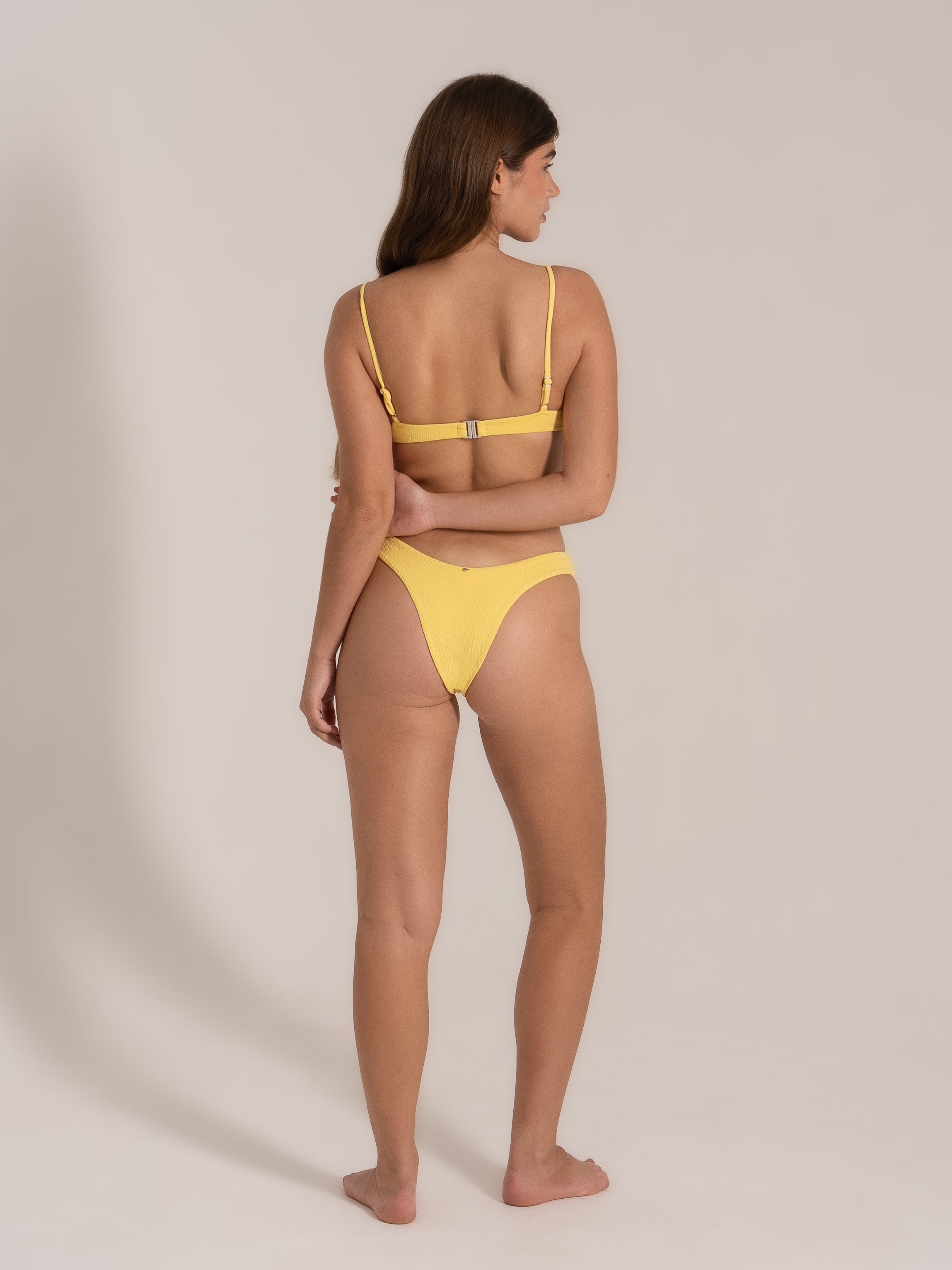  Model from a side-back angle in yellow ribbed bikini featuring a metal back clasp.