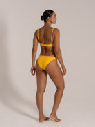 Model showing an angled back view in a yellow textured bikini set with supportive straps and cheeky bottom.