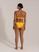 Back view of a model wearing a yellow textured bikini set with halter straps and clasp closure.