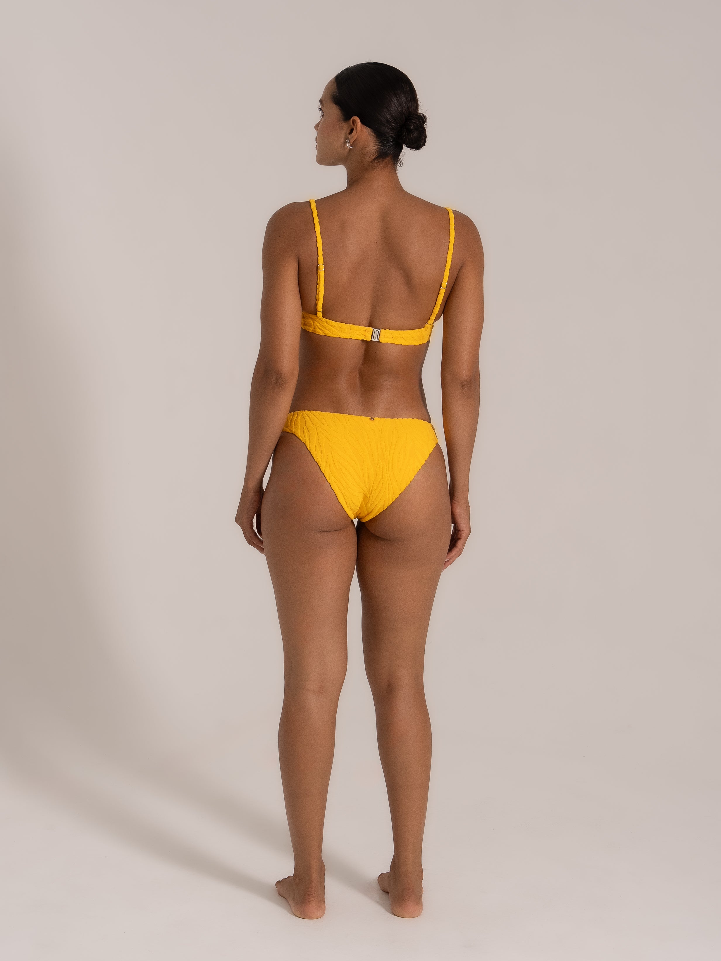 Back view of a model wearing a yellow textured bikini set with halter straps and clasp closure.