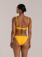 Back view of woman wearing a mustard yellow bikini set with textured fabric, adjustable thin straps, and a clasp closure.