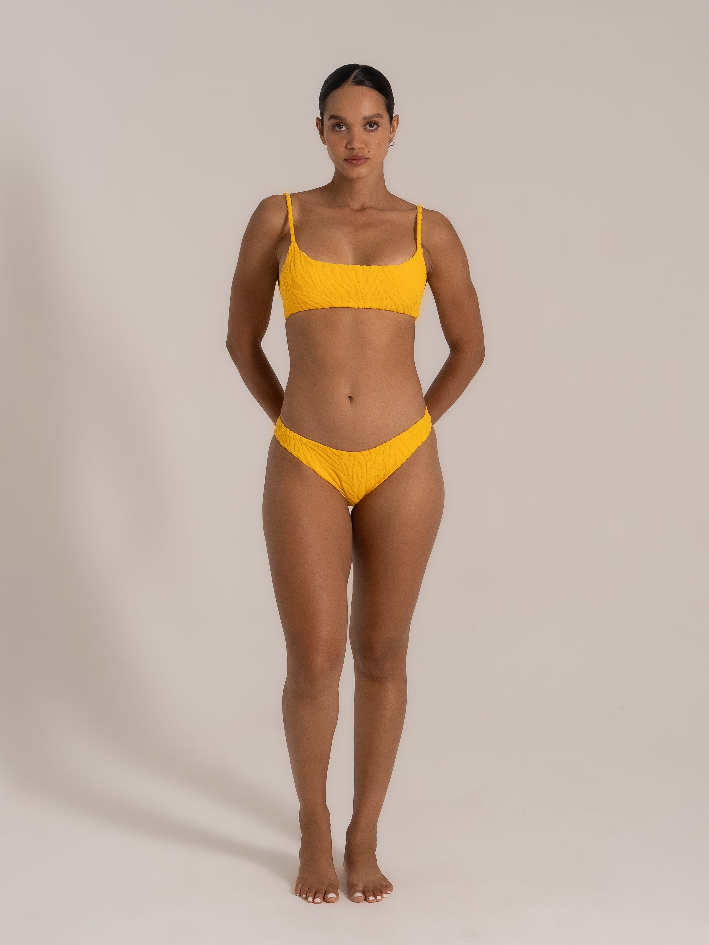 Front view of a model in a yellow textured bikini set with scoop neck top and matching bottom.