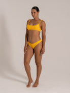 Side front view of a model wearing a yellow textured bikini set with adjustable shoulder straps and low-rise bottom.