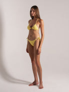 Model in yellow textured bikini with halter top and string tie bottoms, side pose