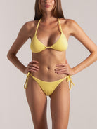 Front view of a woman wearing a yellow textured triangle bikini with halter straps and side tie bottoms.