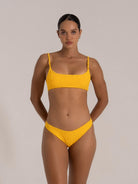 A stylish model in a bright - colored, textured yellow bikini, exuding confidence with a neutral - toned backdrop.